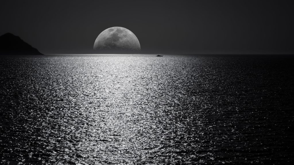 The moon appears over the horizon of a body of water, while a small boat is visible in the shadows at a distance. The moonlight reflects vividly off the waterway.